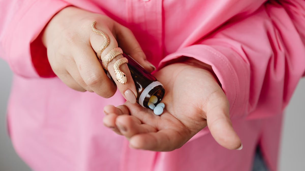 Close-up of hands pouring medicine pills from a bottle, wearing a stylish gold snake ring.